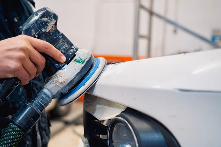 Orbital sander levelling filler along the edge of a white front fender